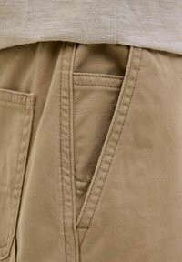 Pantalons khaki avec une texture lisse, dotés de poches latérales et de coutures visibles. Le tissu a une apparence robuste et durable.
