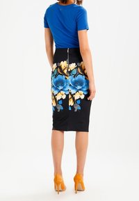 Gonna a matita nera con stampa floreale di fiori blu e gialli, dettaglio di cerniera sul retro; abbinata a una maglia aderente blu e tacchi arancioni.