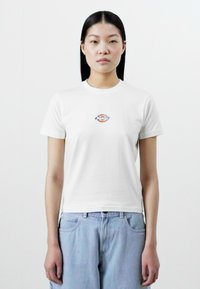 Hvit bomull T-skjorte med rund hals og korte ermer. Har en liten fargerik logo på brystet. Kombinert med lyseblå denim-bukser.