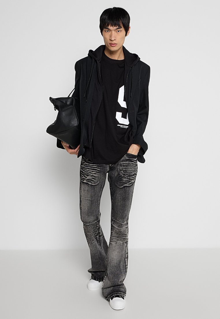Black oversized hoodie layered over a black graphic t-shirt with a white number. Worn with distressed gray jeans and white sneakers.