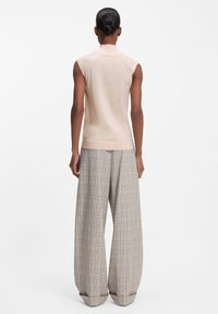 Jasnobeżowy, bezrękawnik z wysokim kołnierzem; połączony z szerokimi spodniami w kratę w odcieniach szarości, brązu i czerwieni, wykonanymi z miękkiego materiału.