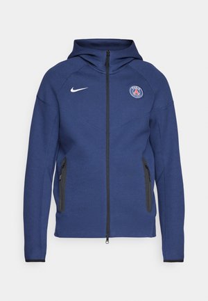 Sudadera con capucha de color azul marino hecha de tela suave, con cierre completo, bolsillos laterales y un parche con logo. Tiene un diseño estructurado con capucha.