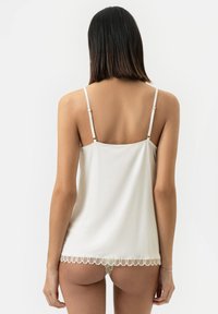 Camisole blanche avec bretelles réglables, dentelle à l'ourlet et texture lisse. Conçue pour un ajustement confortable.
