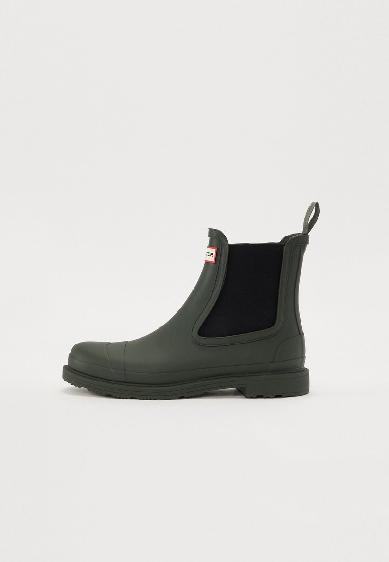 Roheline kummist Chelsea saabas mustade elastsete külgpaneelidega, tekstureeritud tallaga ja hõlpsaks selga panemiseks mõeldud silmus. Esiküljel punane silt.