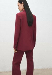 Vínové sako s na míru šitým blejzrem a kalhotami ve stejném odstínu. Hladká látka, strukturovaný design, zdobený manžetami na knoflíky a rozparkem vzadu.