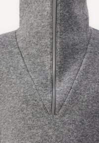 Jersey de fieltro gris con cuello alto, presenta una cremallera frontal y un diseño de escote en V. Textura suave con un aspecto uniforme.