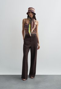 Πολύχρωμη μπλούζα με σχέδιο, παντελόνια καμπάνα σε καφέ ζιγκζαγκ σχέδιο και πλεκτός κάπα με καπέλο τύπου bucket και ταιριαστό κασκόλ. Ομαλές υφές.