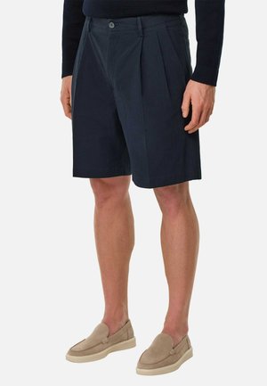 Sømandsblå plisserede shorts lavet af struktureret stof, med knaplukning og sidelommer. Sat sammen med lysebeige slip-on sko.