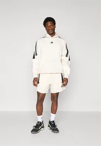 Set din bumbac format din hanorac și pantaloni scurți de culoare alb-crem cu dungi negre. Are un buzunar tip cangur și un logo mic. Purtați cu pantofi sport negri.