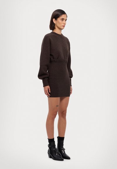 Strikket brun sweaterkjole med lange ærmer, ribbet tekstur, knapdetaljer i taljen, parret med sorte ankelstøvler med spids tå.