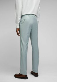 Helleblaue maßgeschneiderte Hose aus strukturiertem Stoff, mit einer Gesäßtasche und Knopfverschluss. Getragen mit braunen Dressschuhen.