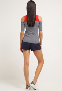 Top de hombros descubiertos a rayas en azul marino y blanco, con hombros rojos, combinado con pantalones cortos azul marino. Presenta un estilo ajustado y mangas cortas.