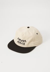 Beige cordfløyelslue med svart skjerm, som har svart brodert tekst "FORMER MERCH" på forsiden. Inneholder en knapp på toppen.