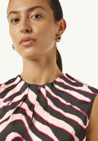 Ärmelloses Kleid mit plissiertem Ausschnitt, das eine schwarze Basis und auffällige pinke und rote gewellte Streifen aufweist. Goldene, kugelförmige Ohrringe runden den Look ab.