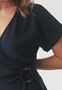 Granatowa sukienka kopertowa z krótkimi rękawami. Posiada wiązanie w talii z akcentem w postaci klamry w kolorze żółwia. Gładka faktura tkaniny.