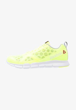 Chaussure de sport Reebok jaune néon avec tige en mesh, motif hexagonal, semelle blanche et logo rouge sur le côté et la languette du talon.