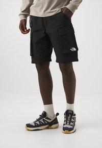 Czarne szorty cargo z wieloma dużymi kieszeniami, luźnym krojem i logo The North Face. W zestawieniu z wielokolorowym obuwiem hikingowym i białymi skarpetkami.