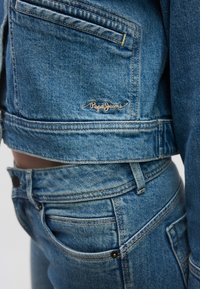 Μπλε τζιν μπουφάν με κροπ σχέδιο, που διαθέτει μπροστινές τσέπες και κεντημένο λογότυπο "Pepe Jeans". Ζεύγος τζιν ψηλόμεσα που ταιριάζουν.