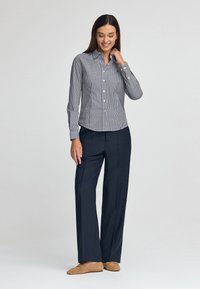 Button-up-Hemd im schwarz-weißen Vichykaro-Muster, kombiniert mit navyblauen weit geschnittenen Hosen. Es verfügt über einen Kragen und lange Ärmel mit Manschetten.
