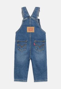 Μπλε τζιν φορμάκι για παιδιά με ρυθμιζόμενους ιμάντες στους ώμους, δύο πίσω τσέπες με ραφές και ένα ταμπελάκι της μάρκας Levi's σε ταμπά χρώμα.