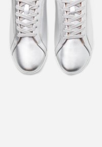Ezüst színű sneakers cipők sima, fényes textúrával, fehér fűzőkkel, kerek orral és minimalista dizájnnal. Nincs látható logó vagy minta.