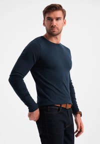 Mörkblå långärmad tröja i jersey med rund halsringning, med ribbade mudd och en smal passform, kombinerad med mörka jeans och ett brunt bälte.