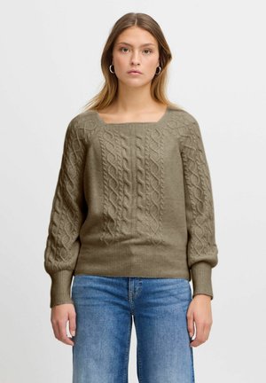 Pull en laine vert olive avec un design en tricot torsadé, encolure carrée et poignets côtelés. Associé à un jean en denim bleu clair.