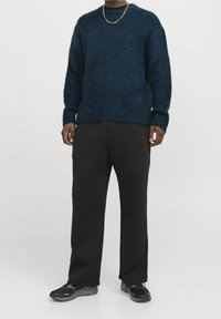 Granatowy sweter z dzianiny o okrągłym dekolcie, luźnym kroju i prążkowanych mankietach, w połączeniu z czarnymi spodniami i czarnymi trampkami.