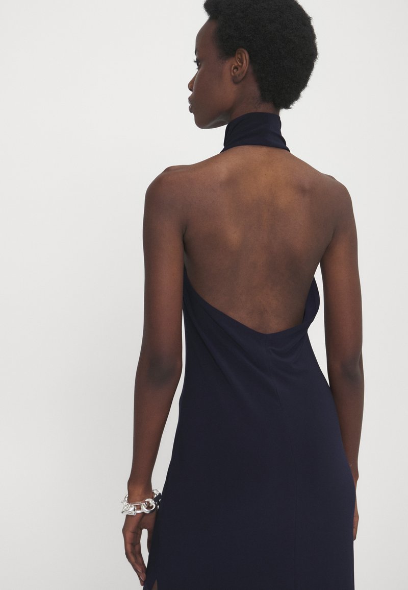 Navyblaues Halterneck-Kleid mit offener Rückseite, ausgestattet mit einem drapierten Design und seitlichem Schlitz, aus glattem, leichtem Stoff gefertigt.