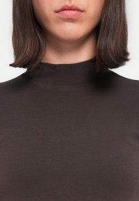 Bruine hoge-nektop met een gladde textuur en een aansluitende silhoeet, met korte mouwen en minimale stiksels rond de halslijn.