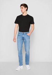 Heledad sinine denim püksid sirge lõikega, koos musta lühikese varrukaga T-särgi ja valgete spordikingadega. Lihtne disain, ilma mustriteta.