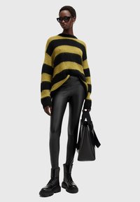 Maglione oversize a righe gialle e nere, leggings in similpelle nera, stivali neri chunky e una borsa tote nera lucida.