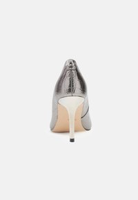 Hallhalli lakitud nahast kingad krokodillimustriga, terav nina ja kõrge stilettokontsaga. Seljal on väike logoaktsent.