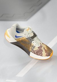 Sport sneaker with grey mesh upper, camouflaged pattern in brown and orange, blue accents, rubber sole, and lacing system for secure fit.