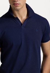 Tmavě modré polotričko s límečkem, krátkými rukávy a nenápadným logem na hrudi. Vyrobeno z texturované tkaniny.