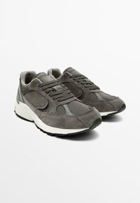 Des baskets en suède gris et en mesh présentent une langue et une collerette rembourrées, des lacets plats, ainsi qu'une semelle intermédiaire texturée blanche avec une semelle extérieure en caoutchouc noir.