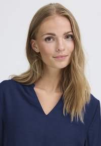 Blusa blu navy con scollo a V, tessuto testurizzato e vestibilità rilassata. Aspetto leggermente stropicciato e maniche lunghe.