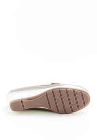 Sneaker con una toma superiore beige chiaro, dettagli metallici e una suola bianca. Suola in gomma marrone testurizzata con scanalature per aderenza e stabilità.