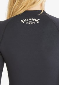 Une combinaison de plongée noire avec une texture lisse et un design classique. Présente un logo Billabong blanc brodé au niveau du cou avec l'année 1973.