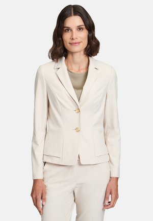 Blazer fitted di un beige chiaro con colletto, due bottoni dorati e tasche laterali. Texture liscia, design su misura e maniche lunghe.