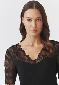 Sort top med korte ærmer, der har detaljer af intrikat blondestof og en scalloped halsudskæring. Glat stof med en tætsiddende form.