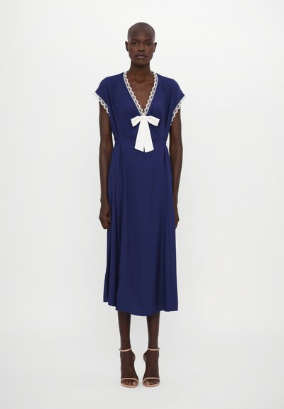 Navy blue dress with a deep V neckline, lace trim, and a white bow detail at the center. It has short sleeves and a flowing silhouette.