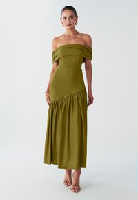 Off-shoulder, olivengrøn maxikjole med rynket overdel, tekstureret stof og sideløb. Bær med beige sandaler med hæl.