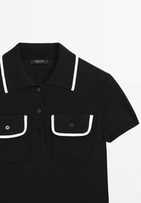 Polo noir à manches courtes avec bordure blanche sur le col et les rabats des poches, doté de trois boutons sur le devant et de deux poches poitrine à boutons.