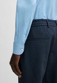 Camicia a righe blu chiaro con bottoni bianchi, abbinata a pantaloni texture blu navy scuri con tasca posteriore.