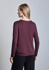 Bordeauxrotes Langarmshirt mit weitem Ausschnitt, lockerer Passform und glatter Textur. Verfügt über einen geraden Saum und gerippte Bündchen.