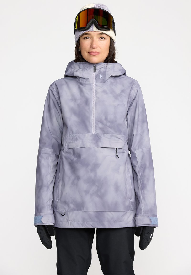 Chaqueta de esquí de color púrpura claro con un diseño estampado, capucha ajustable, cremallera frontal y puños elásticos. Se lleva con gafas de esquí y guantes.
