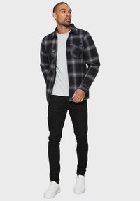 Eine schwarz-grau karierte Flanellhemd über einem grauen T-Shirt, kombiniert mit schwarzen Hosen und weißen Sneakern. Verfügt über Knopftaschen und einen Kragen.