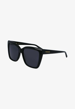 Gafas de sol de gran tamaño en color negro con un marco grueso y lentes oscuros. Presenta un detalle del logotipo en oro en el lateral. Material de plástico suave con un diseño angular.