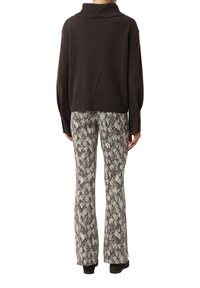 Brązowy krótki sweter z wysokim kołnierzem, zestawiony z rozszerzanymi spodniami z motywem wężowej skóry w kremowo-brązowych odcieniach. Dzianinowy, teksturowany detal.